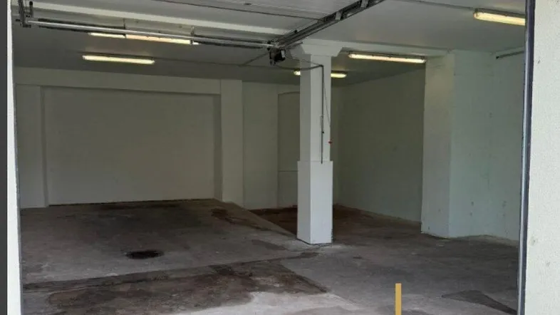 Geräumige Tiefgarage mit Betonboden und automatischem Sektionaltor, ideal für mehrere Fahrzeuge.