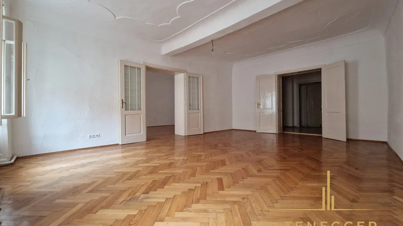 Geräumiges Wohnzimmer mit Fischgrätparkett, hohen Decken und dekorativer Stuckdecke.