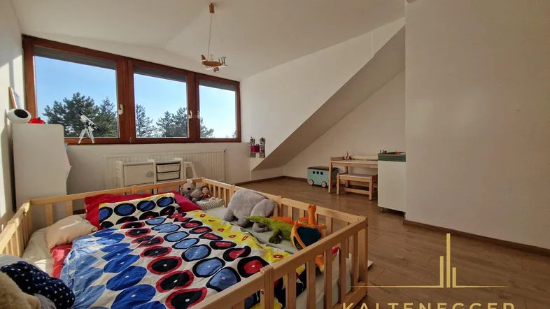 Helles Kinderzimmer im Dachgeschoss mit Holzboden, großen Fenstern und Spielbereich.