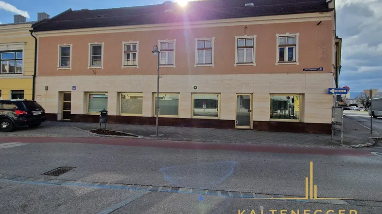 Ansicht der Gebäudefassade mit großen Schaufenstern und einer hellbraunen Verkleidung im Erdgeschoss.