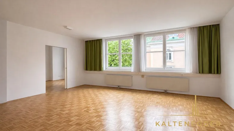 Helles Wohnzimmer mit Parkettboden und großen Fenstern, die viel Tageslicht hereinlassen.