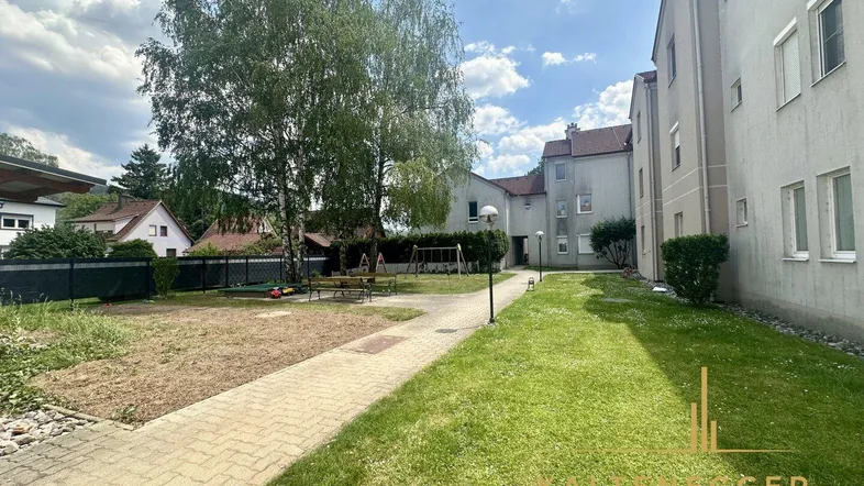 Gemeinschaftlicher Gartenbereich mit Rasenfläche, Spielplatz und Bäumen zwischen den Wohngebäuden.