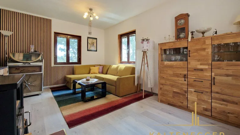 Gemütliches Wohnzimmer mit gelbem Ecksofa, Holzboden und dekorativer Wandverkleidung.