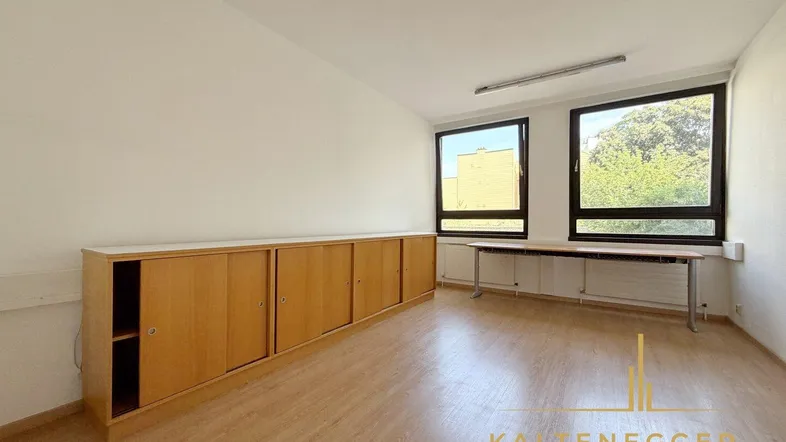 Geräumiges Büro mit hellen Holzschränken, großen Fenstern und Blick ins Grüne.