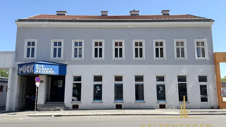 Historisches Gebäude mit grauer Fassade und vielen Fenstern an einer belebten Straße gelegen.