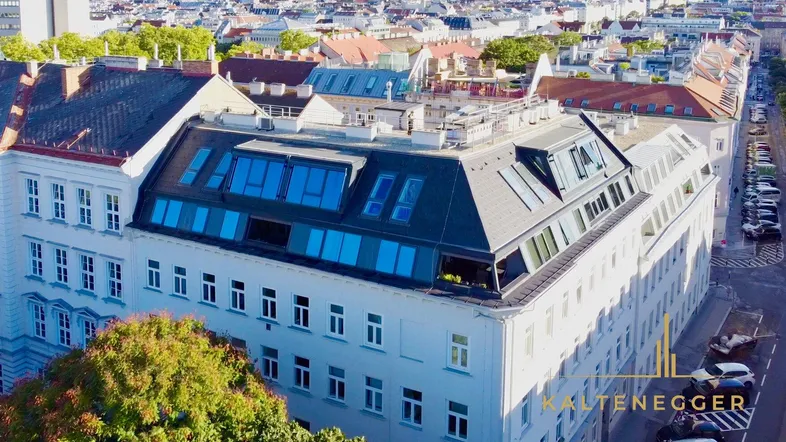 Luftaufnahme eines Gebäudes mit modernem Dachausbau und Mansarddach in urbaner Umgebung.