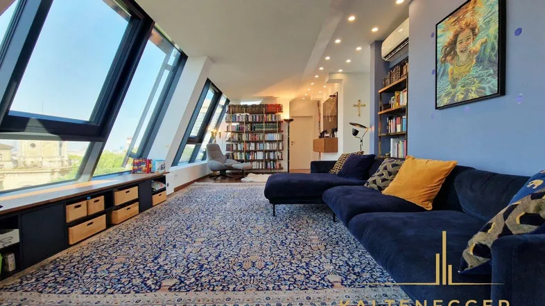 Großzügiges Wohnzimmer mit blauer Couch, Bücherregalen und schrägen Fenstern.
