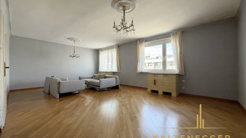 Geräumiges Wohnzimmer mit Parkettboden, eleganten Kronleuchtern und großen Fenstern, die viel Licht hereinlassen.