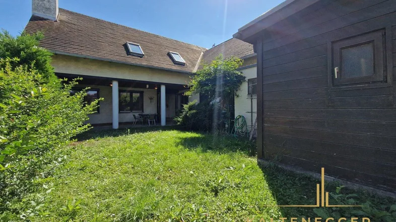 Hinterer Gartenbereich mit Rasenfläche, überdachter Terrasse und Blick auf das Haus.