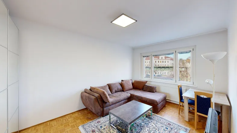 Helles Wohnzimmer mit braunem Ecksofa, Couchtisch und Esstisch am Fenster.