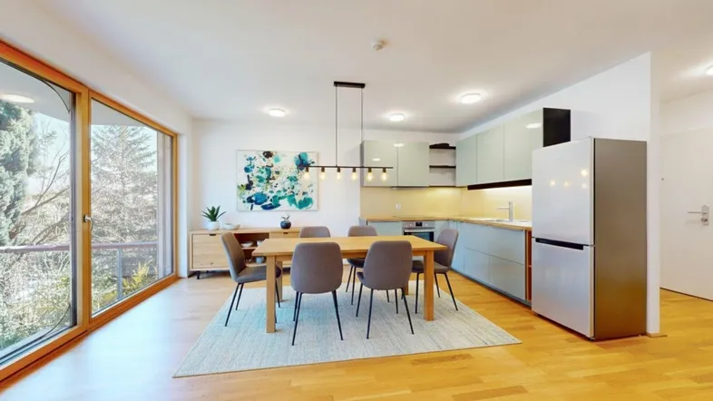 Moderner Wohn-Essbereich mit integrierter Küche, Parkettboden und Zugang zum Balkon.