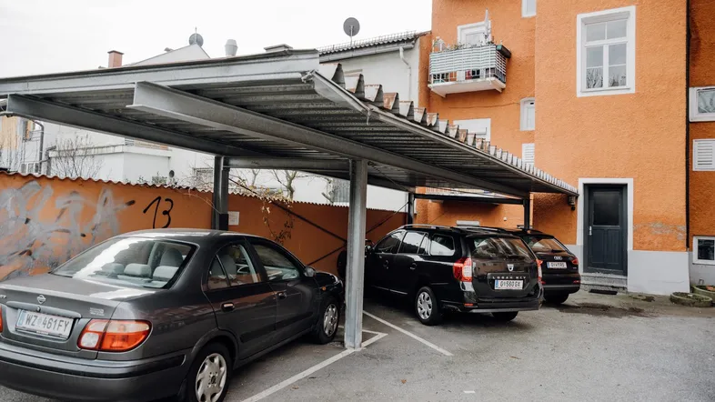 Außenbereich mit überdachten Parkplätzen und orangefarbener Gebäudefassade.