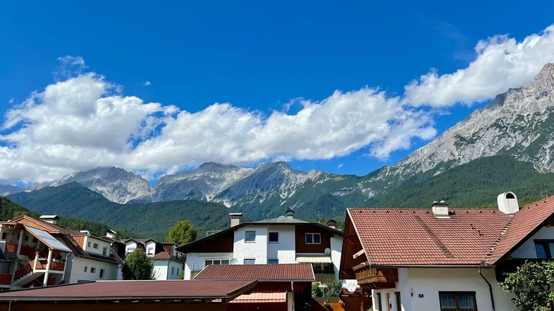 Panoramablick auf eine Wohnsiedlung mit traditionellen Häusern vor einer beeindruckenden Bergkulisse.