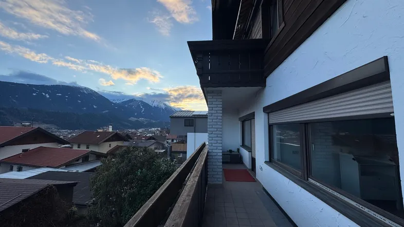 Langer Balkon mit Fliesenboden und Holzbalkonbrüstung, bietet einen weiten Blick auf die umliegende Berglandschaft.