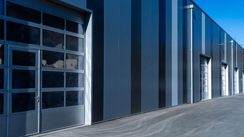 Moderne Industriefassade mit vertikalen Streifen und großen Sektionaltoren aus Glas.