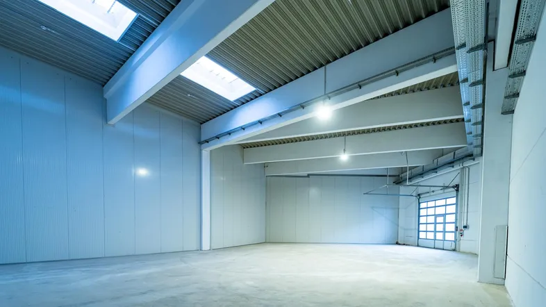 Geräumige, leere Lagerhalle mit hohen Decken, Betonboden und Oberlichtern für natürliches Licht.