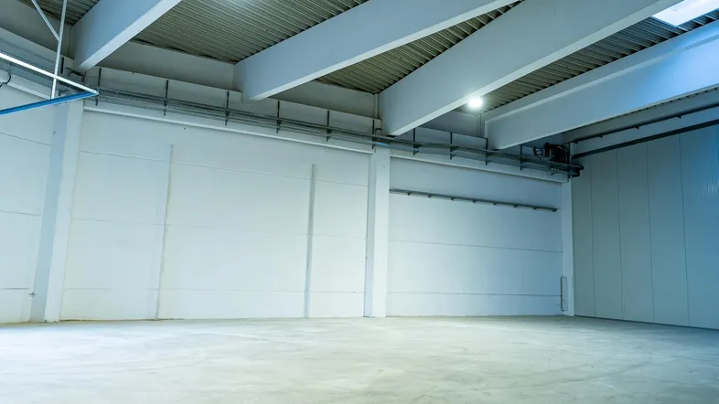 Geräumige, leere Lagerhalle mit hohen Decken, Betonboden und natürlichem Lichteinfall durch Oberlichter.
