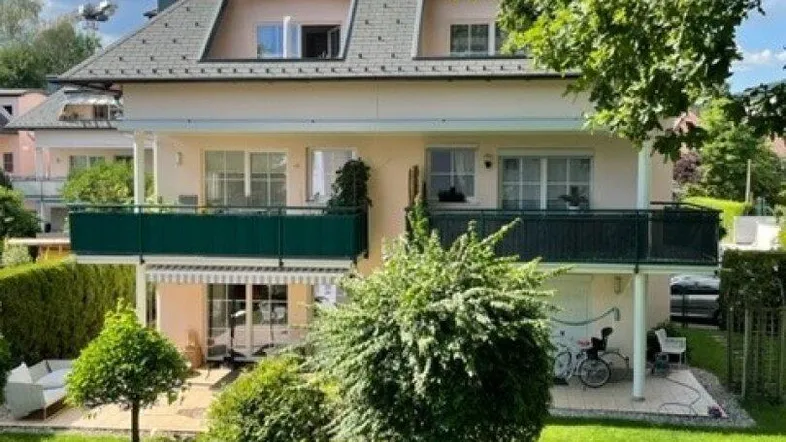 Mehrstöckiges Wohnhaus mit mehreren Balkonen, gepflegtem Garten und üppiger Hecke im Vordergrund.