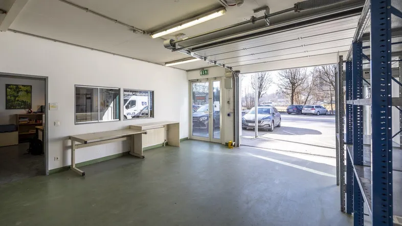 Geräumiger Werkstatt- oder Garagenbereich mit Rolltor, Betonboden und Blick auf den Außenbereich.