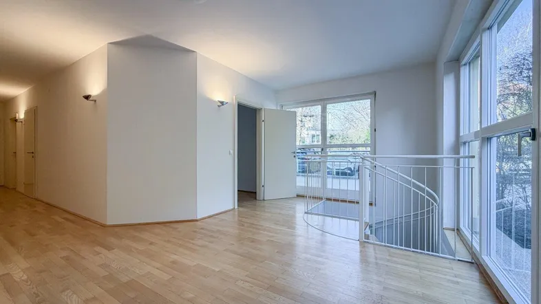 Heller Flur mit Holzfußboden, großen Fenstern und einer Wendeltreppe, die in eine andere Etage führt.