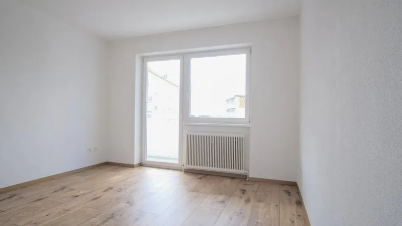 Helles Zimmer mit Holzboden und großem Fenster, bereit zur individuellen Gestaltung.