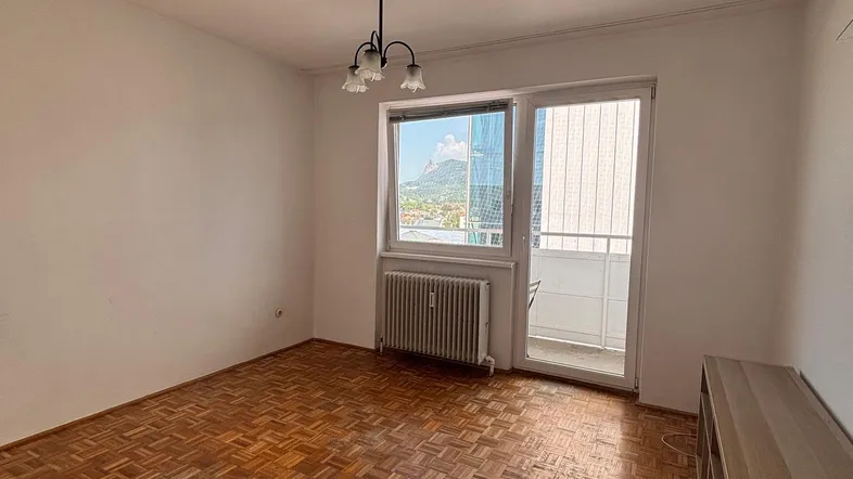Helles Wohnzimmer mit Fischgrätparkettboden und Zugang zu einem kleinen Balkon.
