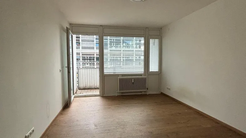 Helles Zimmer mit Holzboden, weißen Wänden und Zugang zu einem Balkon.