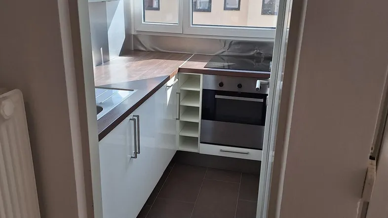 Kleine, funktionale Küche mit Einbaugeräten, Fenster und Blick auf umliegende Gebäude.