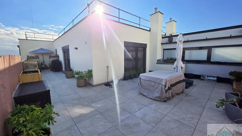 Große Dachterrasse mit Fliesenboden, Pflanzen und einem überdachten Whirlpool unter strahlendem Himmel.