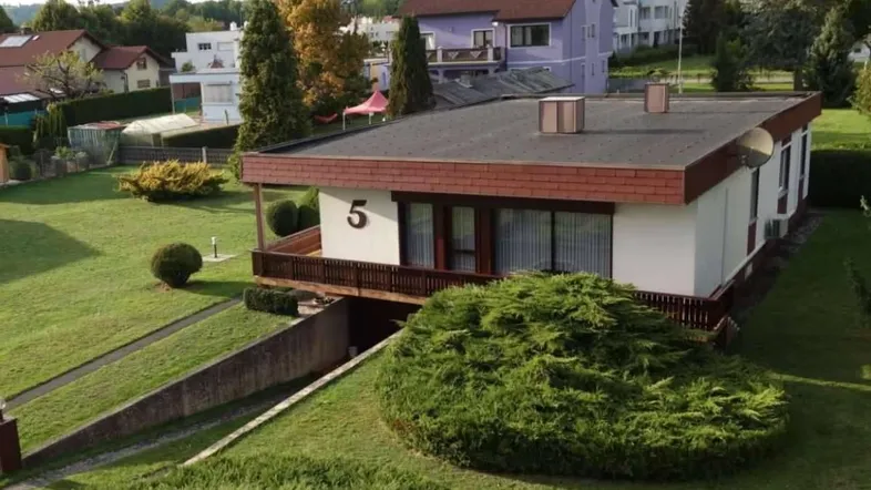 Einfamilienhaus mit Flachdach, Balkon und Garten in einer Wohnsiedlung mit umliegenden Häusern.