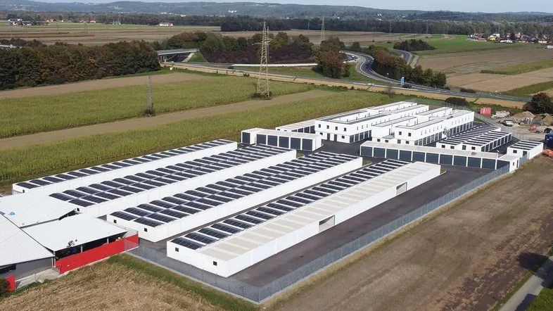 Luftaufnahme einer modernen Garagenanlage mit Photovoltaikanlagen auf den Dächern, umgeben von Feldern.