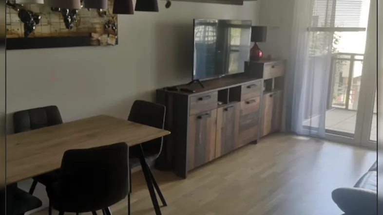 Heller Wohn- und Essbereich mit Holzboden, modernem Mobiliar und Zugang zu einem Balkon.