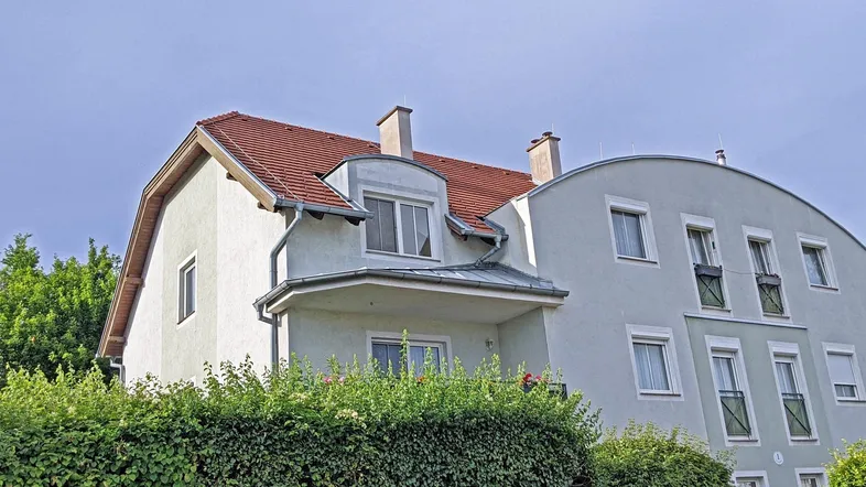 Gebäudeansicht mit Satteldach, Gaube und gepflegter Hecke im Vordergrund.