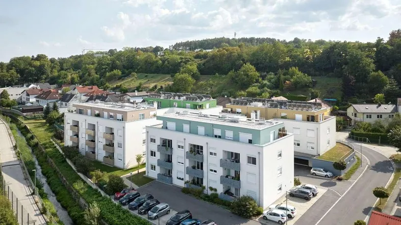 Moderne Wohngebäude in grüner Umgebung mit Parkplätzen und Blick auf bewaldete Hügel.