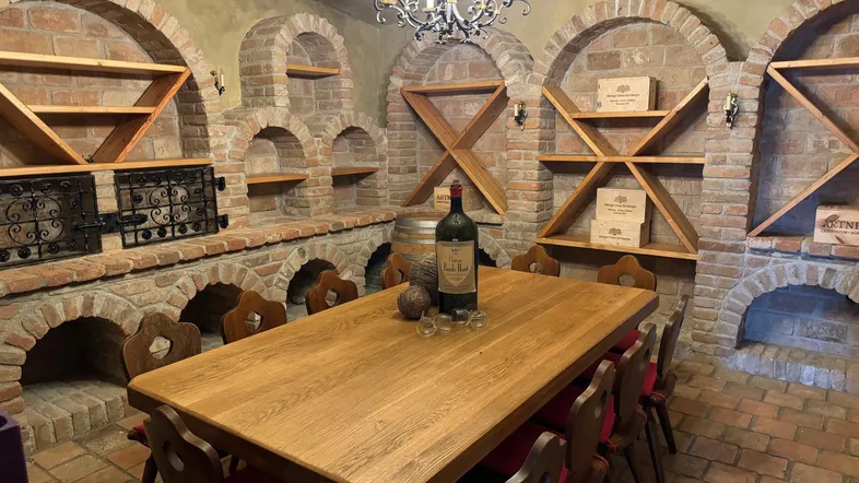 Rustikaler Weinkeller mit großem Holztisch, Ziegelgewölben und Holzregalen für Weinflaschen.