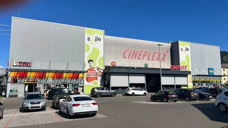 Außenansicht eines modernen Einkaufszentrums mit verschiedenen Geschäften und einem großen Parkplatz.