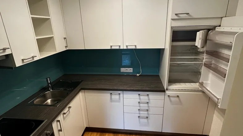 Helle Küche mit weißen Schränken, dunkler Arbeitsplatte, tealfarbener Rückwand und Laminatboden.