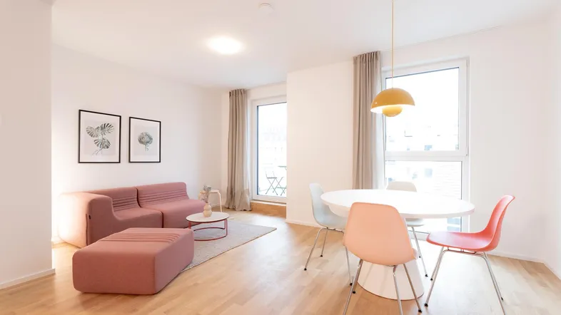 Heller Wohn- und Essbereich mit modernem rosa Sofa, Holzboden und großen Fenstern.
