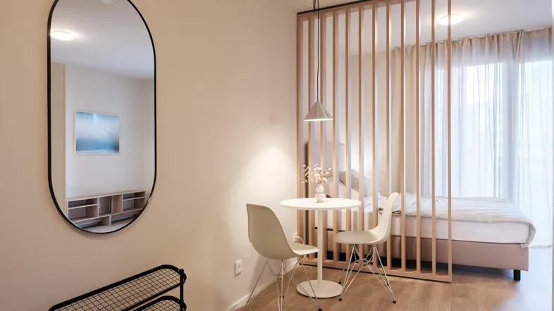 Modernes Studio-Apartment mit Schlafbereich, Essplatz und heller Einrichtung, durch Holzlamellen getrennt.