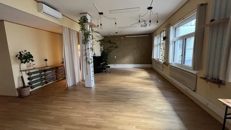Geräumiger Mehrzweckraum mit Holzfußboden, großen Fenstern und Klimaanlage, ideal für verschiedene Aktivitäten.