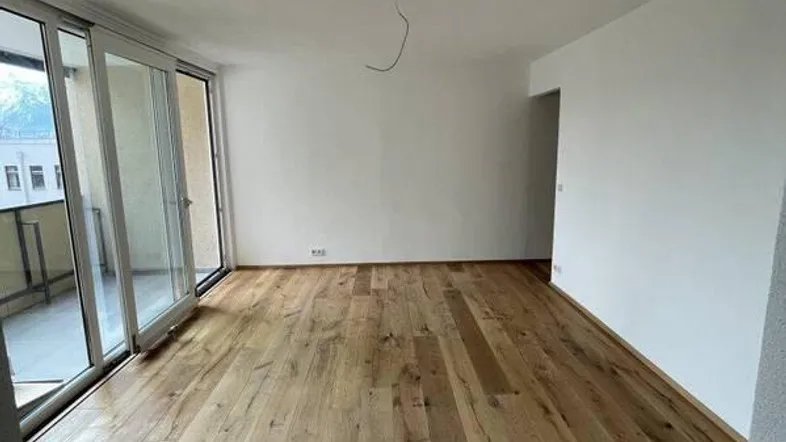 Helles Zimmer mit neuem Holzboden und großen Schiebetüren, die auf einen Balkon führen.