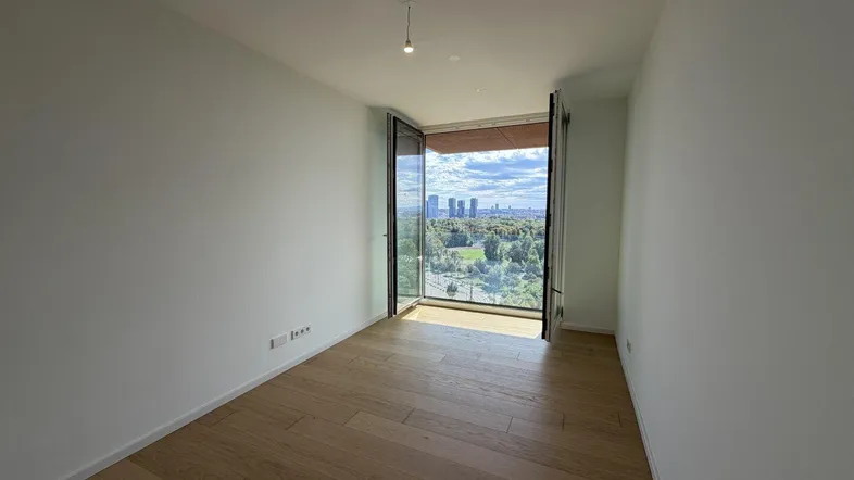 Heller Raum mit Holzboden und großen Fenstern, die einen weiten Blick ins Grüne und auf die Stadt bieten.