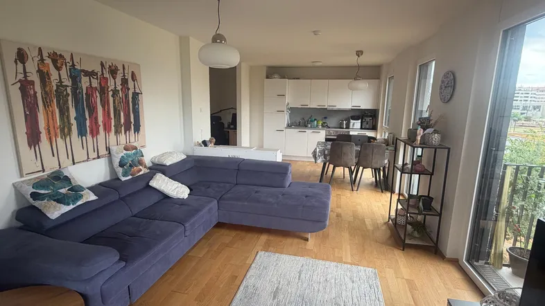 Geräumiger offener Wohn- und Essbereich mit bequemer Couch, Holzboden und Zugang zum Balkon.