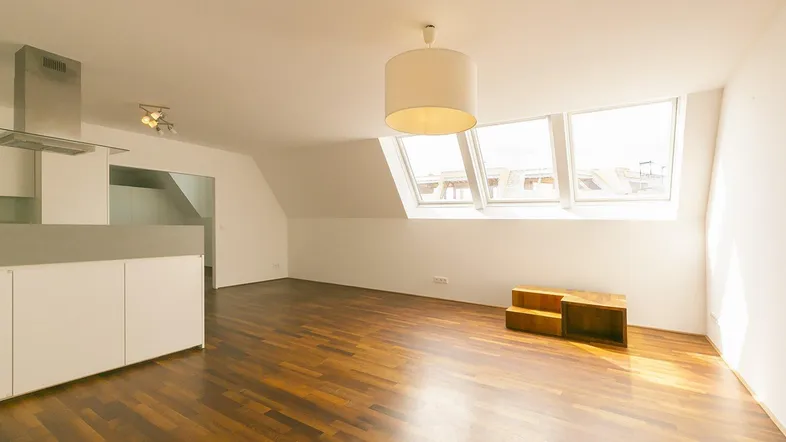 Helles, offenes Wohnzimmer mit integrierter Küche, Holzboden und Dachfenstern, die viel Licht hereinlassen.