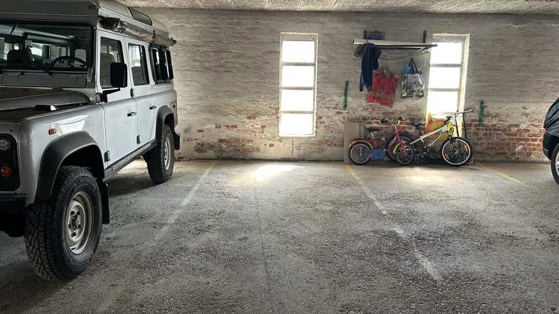 Geräumige Tiefgarage mit Betonboden, Ziegelwänden und abgestellten Fahrrädern neben einem Geländewagen.