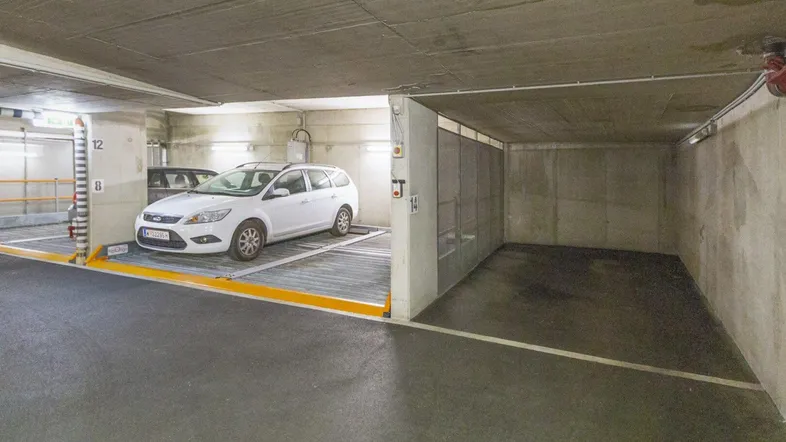 Tiefgaragenstellplatz mit einem weißen Kombi auf einem modernen Auto-Lift-System in einem gepflegten Zustand.