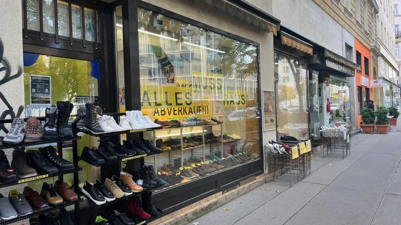 Straßenansicht eines Schuhgeschäfts mit Auslage und Ausverkaufsschildern in einem Altbau.