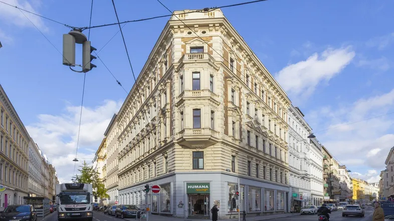 Historisches Eckgebäude mit klassischer Architektur und Geschäften im Erdgeschoss unter blauem Himmel.