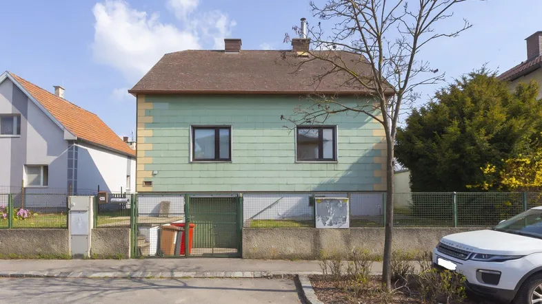 Einfaches Einfamilienhaus mit grün-gelber Fassade und Satteldach in ländlicher Umgebung.