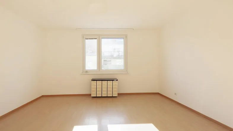 Helles, leeres Zimmer mit Laminatboden und einem Fenster, das viel Tageslicht hereinlässt.